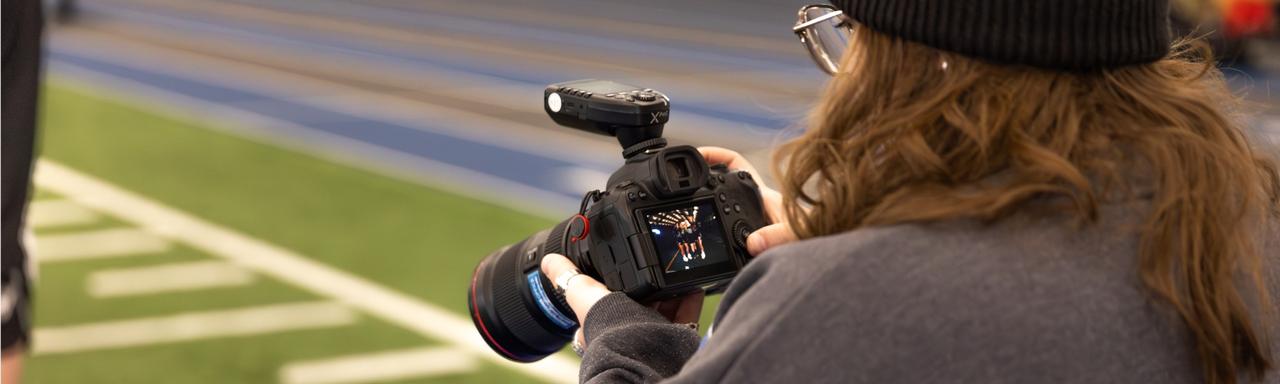 A student photographer looking at photos on her camera while standing on turf